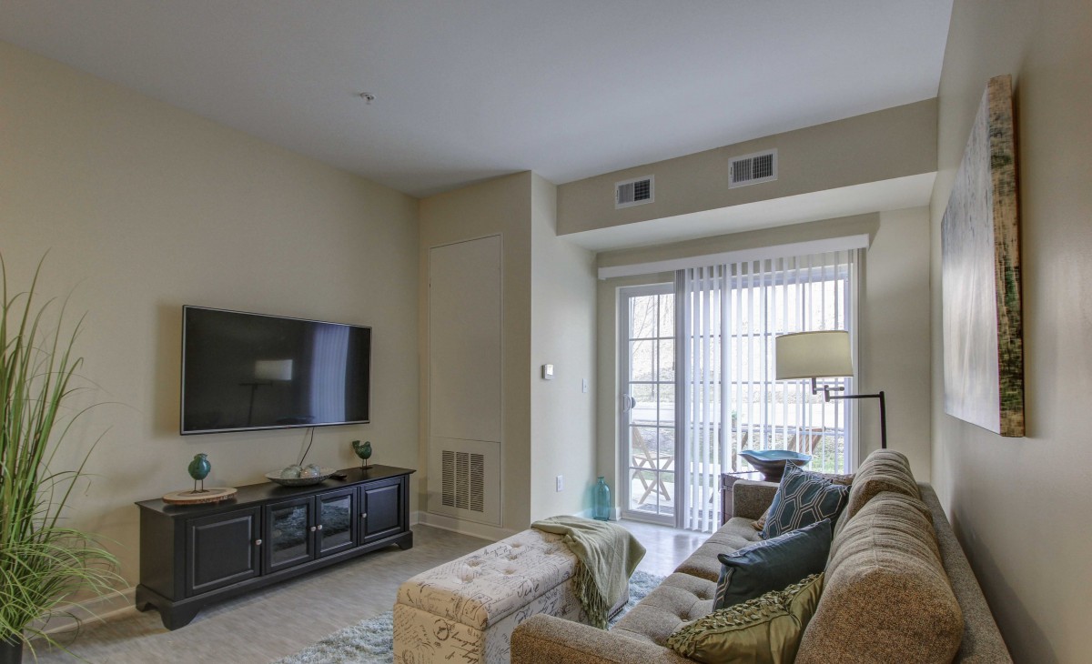 A cozy living room with a sofa facing a wall-mounted TV and a sliding glass door leading outside.
