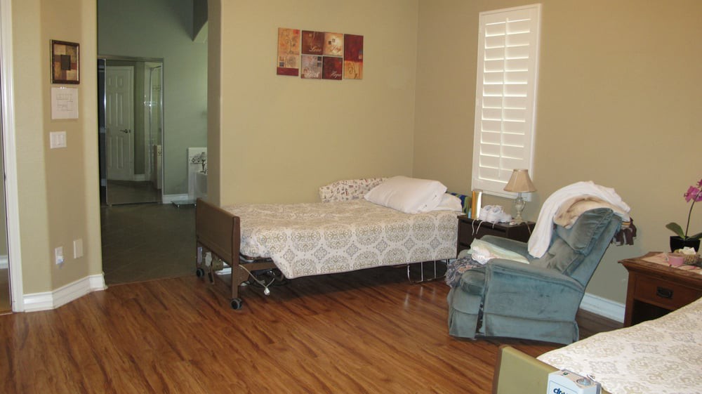 A cozy room with a hospital bed, armchair, and wooden flooring.