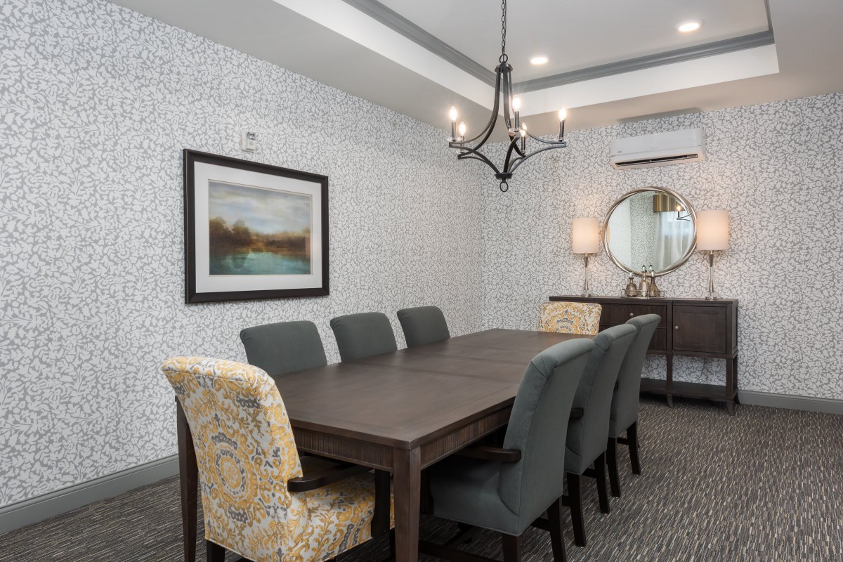 A modern dining room with a long wooden table, upholstered chairs, a stylish chandelier, and decorative wall art and mirror.
