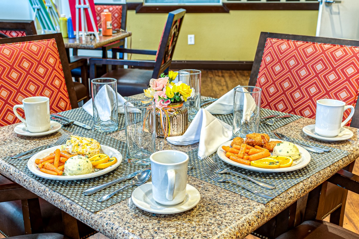 A dining table set for breakfast with plates, cups, and decorative flowers.