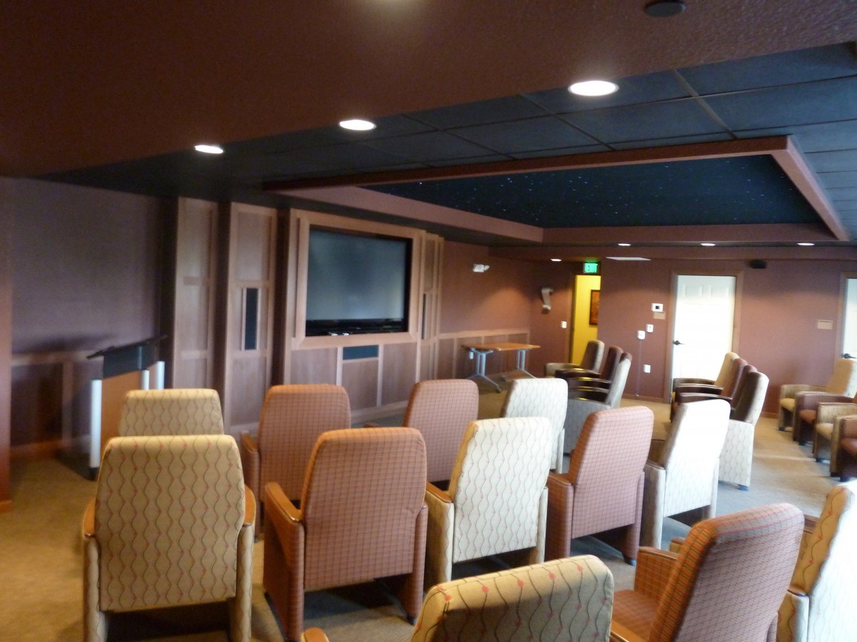 A cozy conference room with arranged seating facing a large screen.
