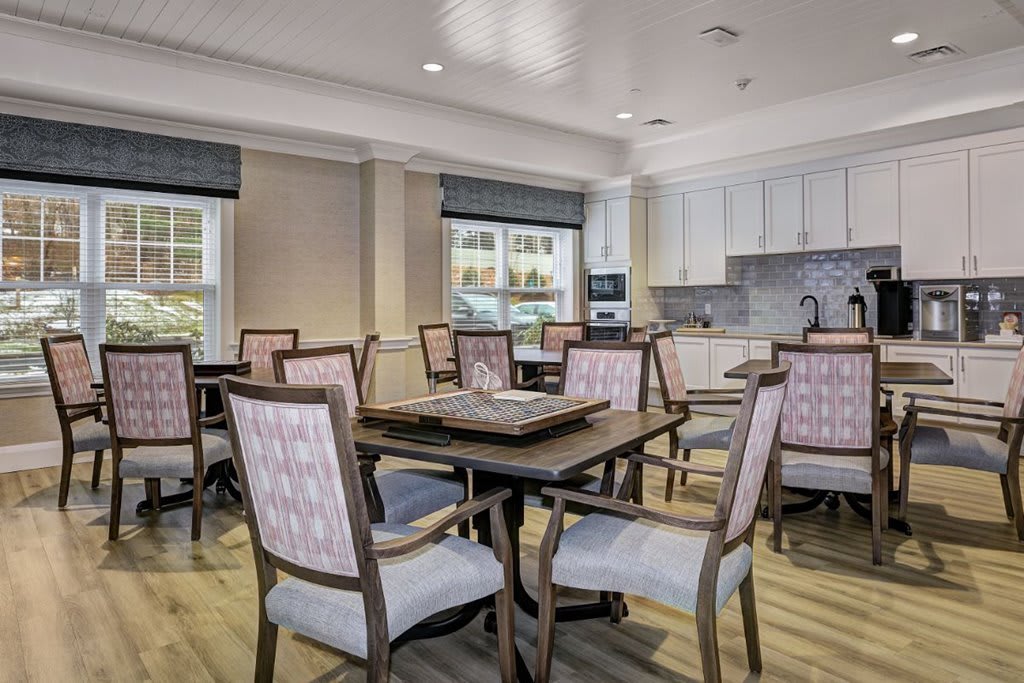 A well-lit dining area featuring multiple tables and chairs, adjacent to a kitchenette.