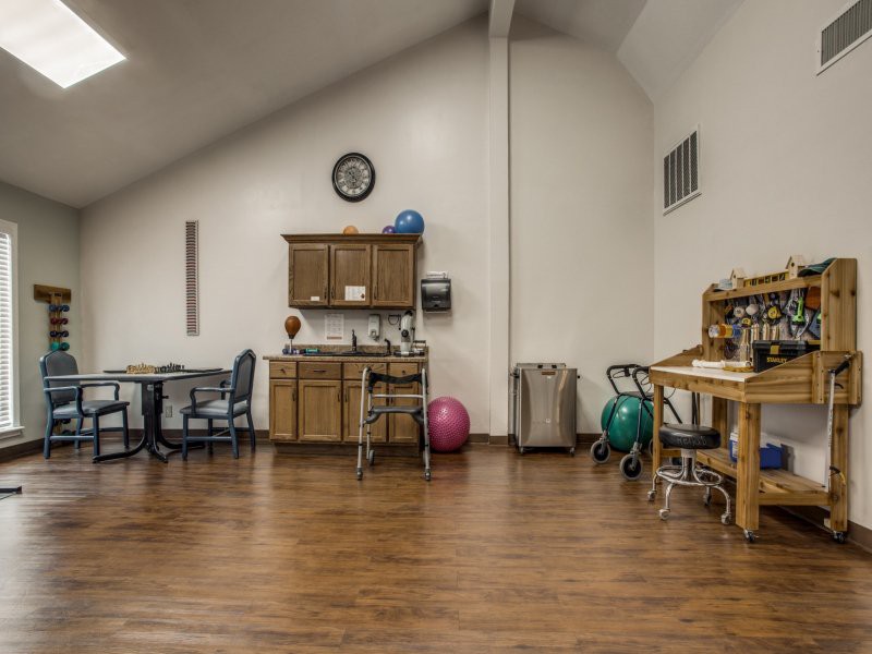 A room equipped with therapy and exercise equipment, including chairs, tables, and exercise balls.