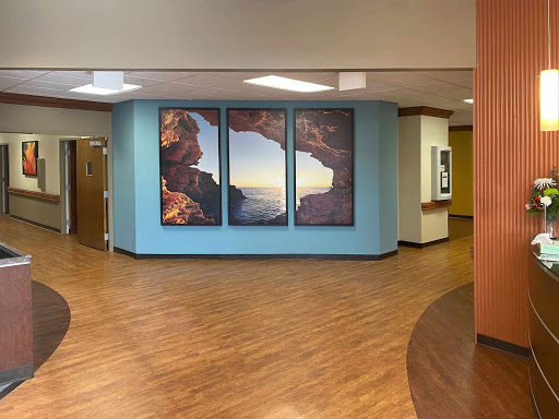 A welcoming hospital lobby featuring large landscape artwork and a warm wooden floor.
