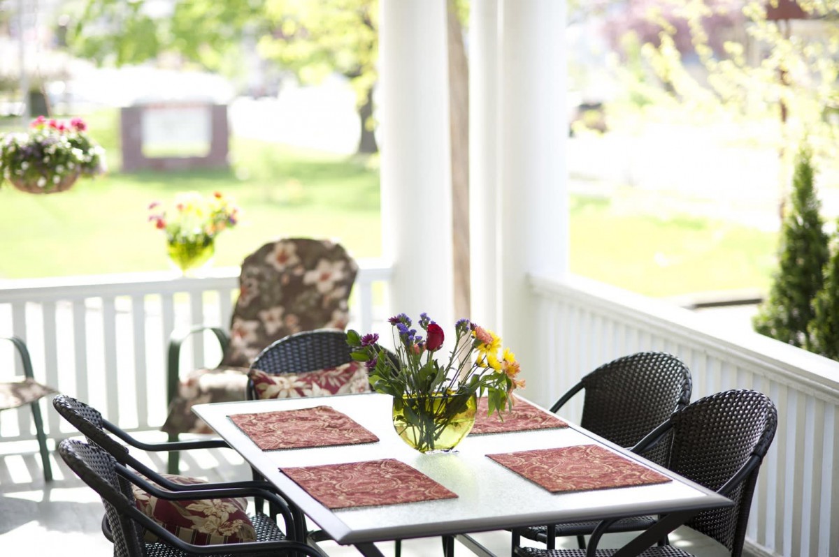 A cozy porch area with a table, chairs, and a vase of flowers.