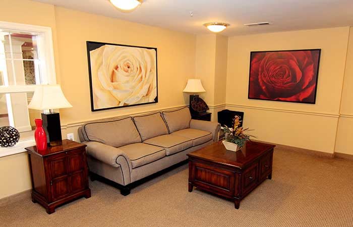 A cozy living room with a sofa, wooden tables, decorative lamps, and floral artwork on the walls.