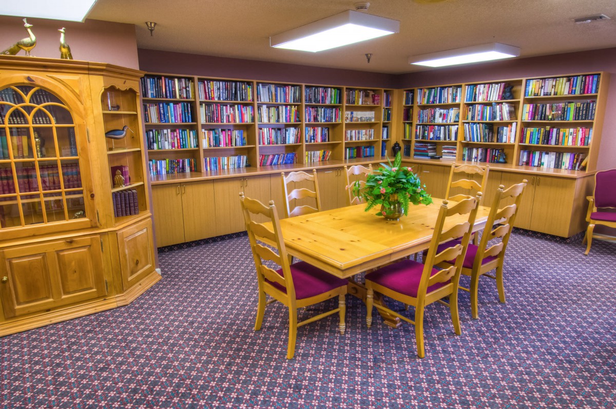 A cozy library room with wooden furniture and bookshelves filled with numerous books.