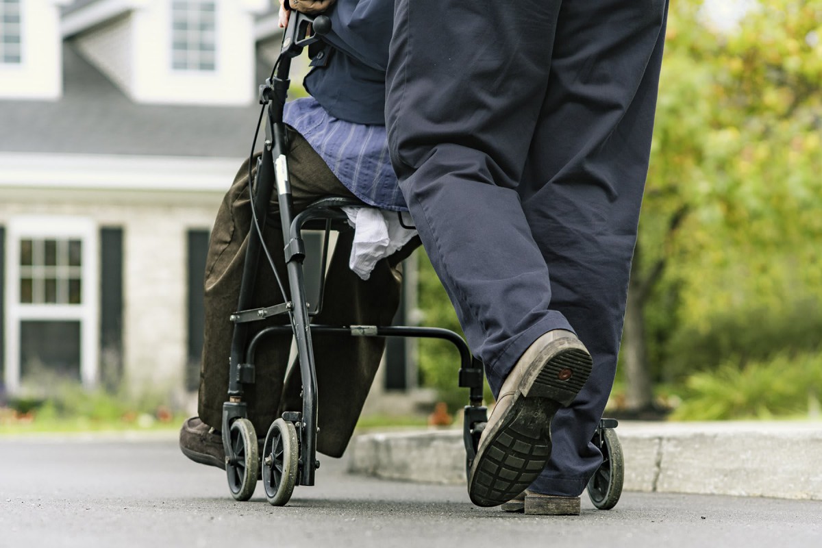 A caregiver assisting an elderly person in a wheelchair outdoors.