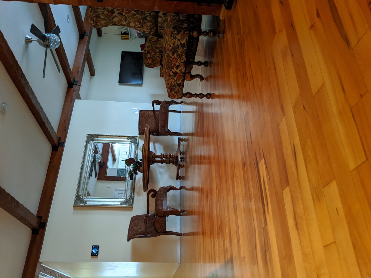 A dining room with a wooden floor, table, and chairs, featuring a large mirror on the wall.
