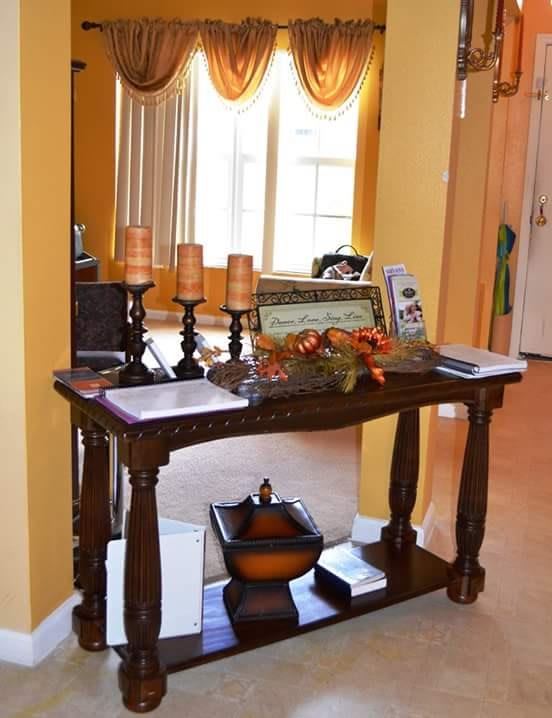 A console table in a living room decorated with candles, framed pictures, and a floral arrangement.