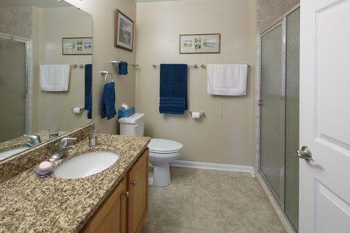 A modern bathroom featuring a sleek design with a granite countertop, neatly arranged towels, and a glass shower.