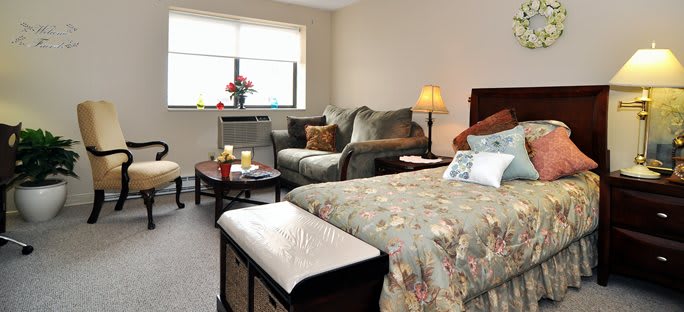 A cozy bedroom with a bed, sofa, and lamp near a window.