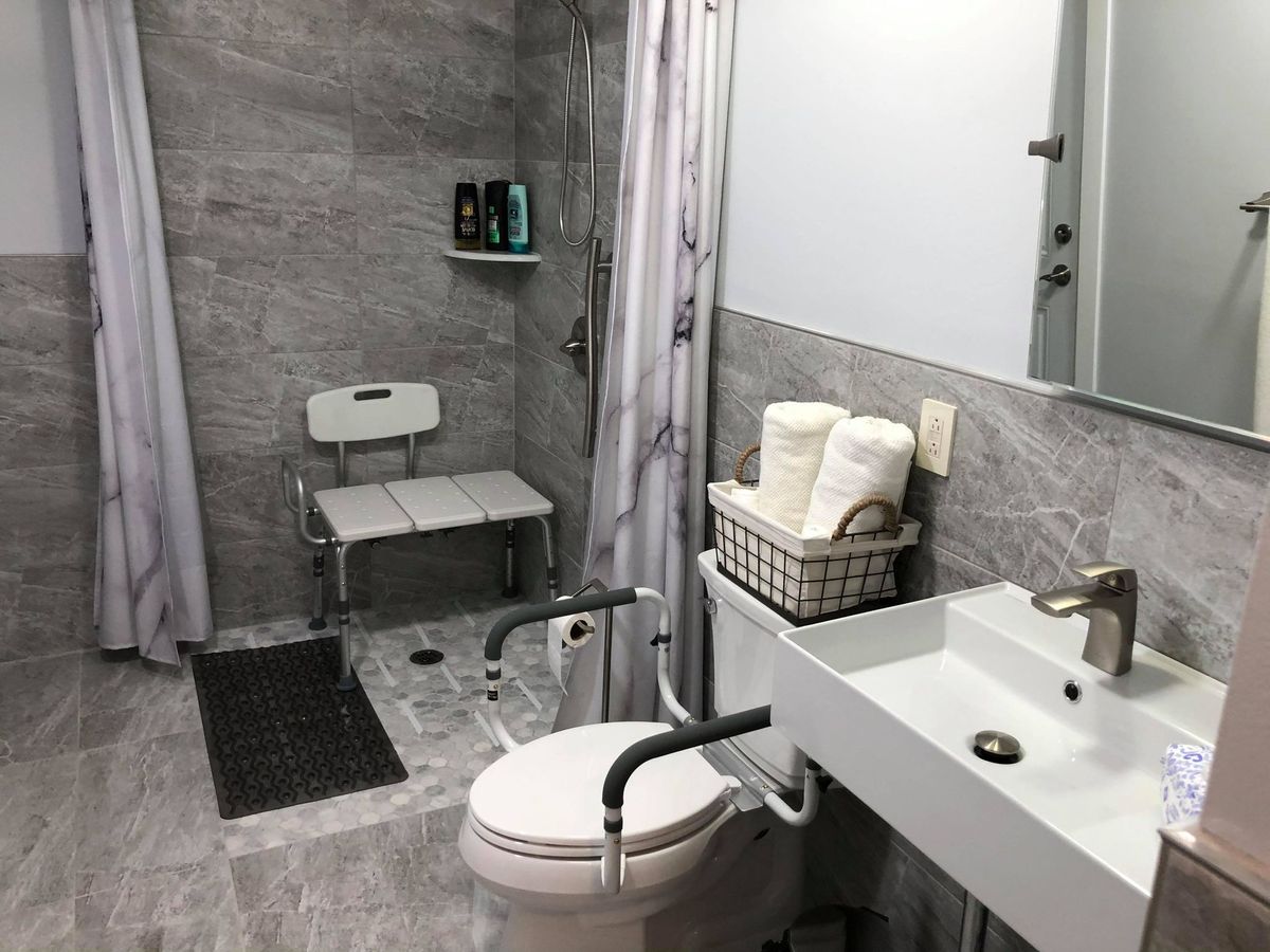 A modern, accessible bathroom featuring a shower chair and grab bars.