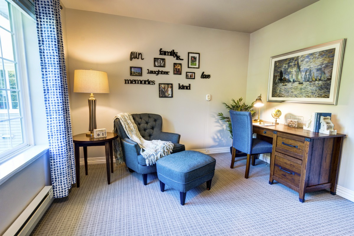 A cozy living room with a comfortable chair, ottoman, desk, and decorative wall art.