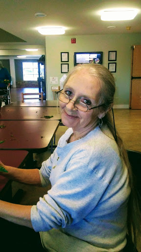 A smiling woman wearing glasses and a casual sweater, seated indoors.
