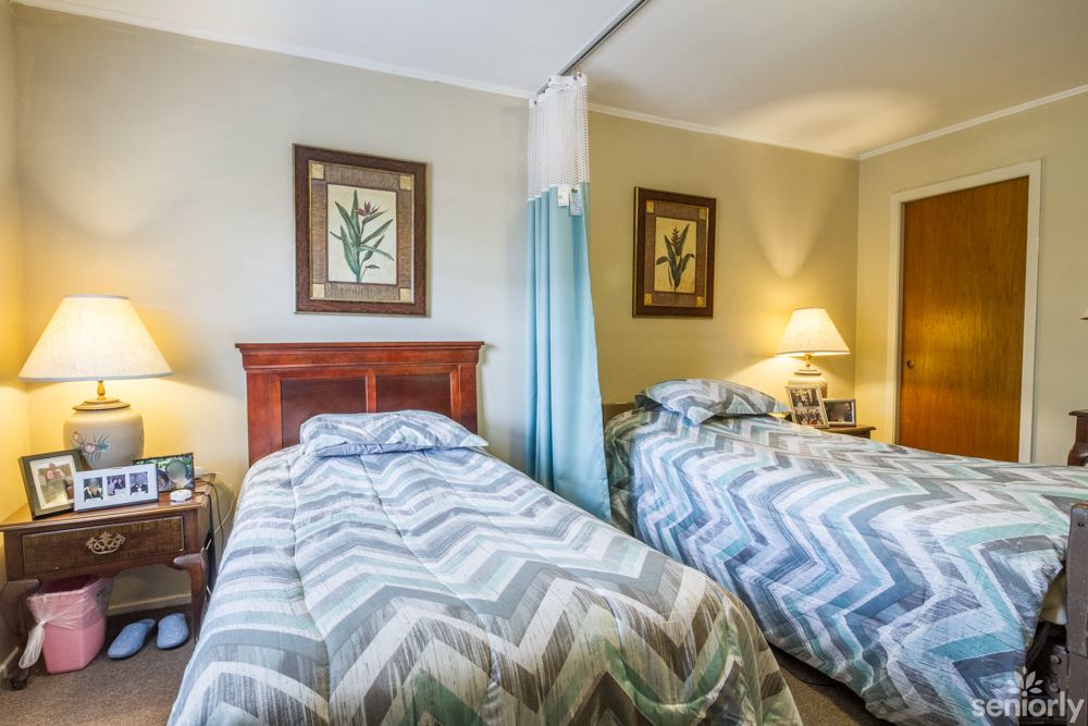 A cozy bedroom featuring twin beds with matching bedding, soft lighting from a bedside lamp, and framed art on the walls.