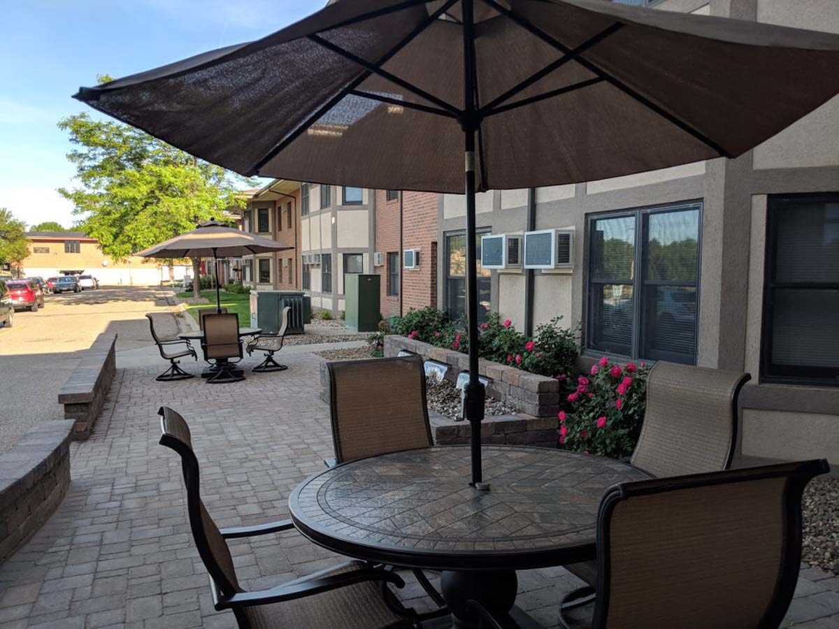 Outdoor patio area with tables, chairs, and umbrellas near a building.