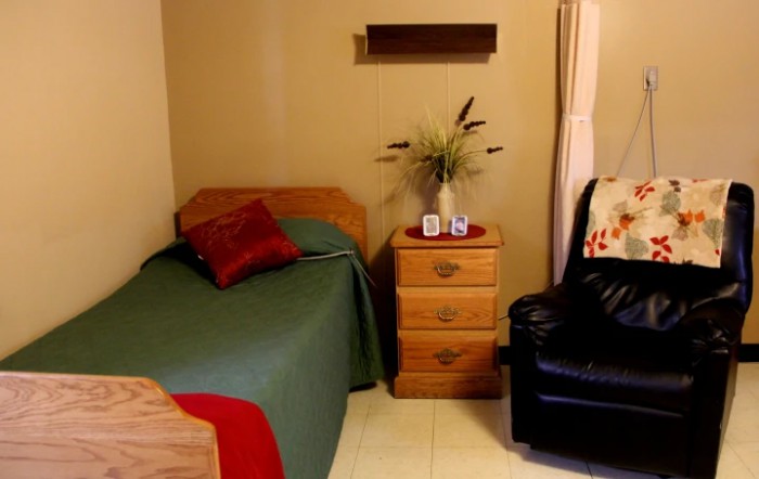 A cozy bedroom with a single bed, nightstand, and a comfortable chair.