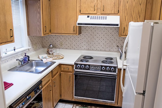 A small kitchen featuring a stove, oven, sink, and refrigerator with wooden cabinets.