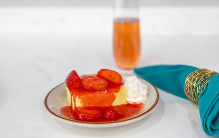 A slice of cheesecake topped with strawberries and whipped cream, served with a refreshing drink.