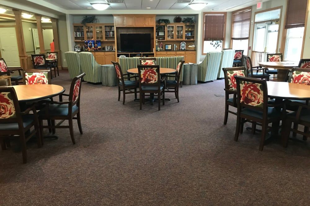 A spacious living room area with multiple tables and chairs, a television, and shelves in the background.