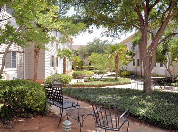 A serene courtyard garden with trees, bushes, and outdoor seating.