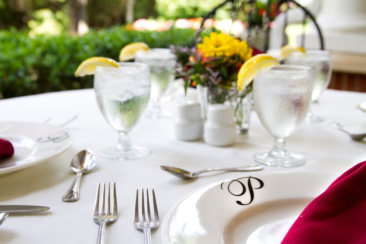 A beautifully arranged outdoor table set for a formal dining experience, featuring elegant glassware and floral decorations.