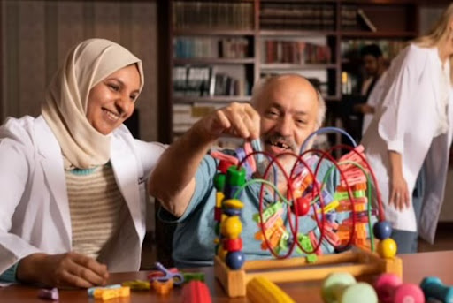 A caregiver engages with an elderly man in interactive play using colorful wooden toys, promoting cognitive and emotional wellness.