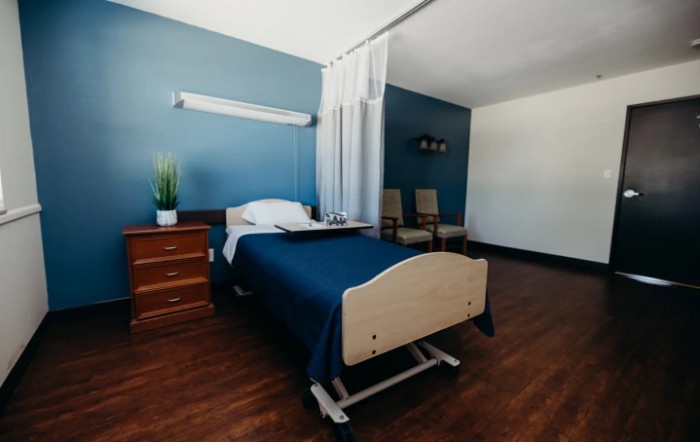 A clean and minimalist hospital room with a single bed and wooden flooring.
