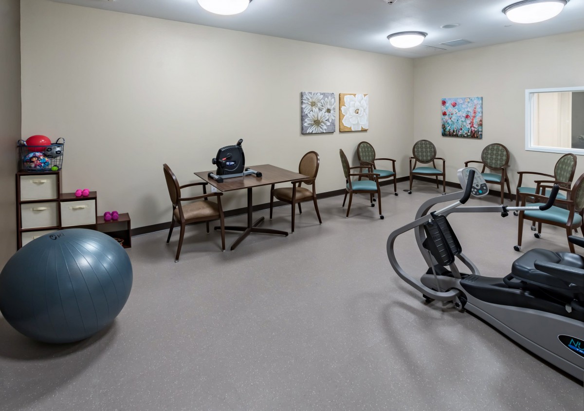 A small exercise room with gym equipment, chairs, a table, and a fitness ball.