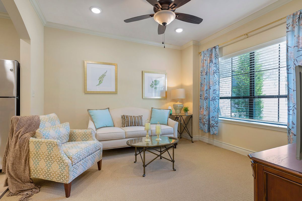 A cozy living room with a sofa, armchair, and coffee table, featuring light decor and a ceiling fan.