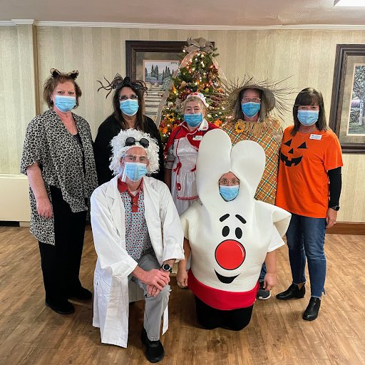 A festive group dressed in creative costumes poses for a Halloween-themed photo in front of a decorated tree.