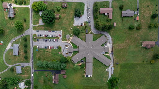 An aerial view of a building complex surrounded by greenery and a parking area.