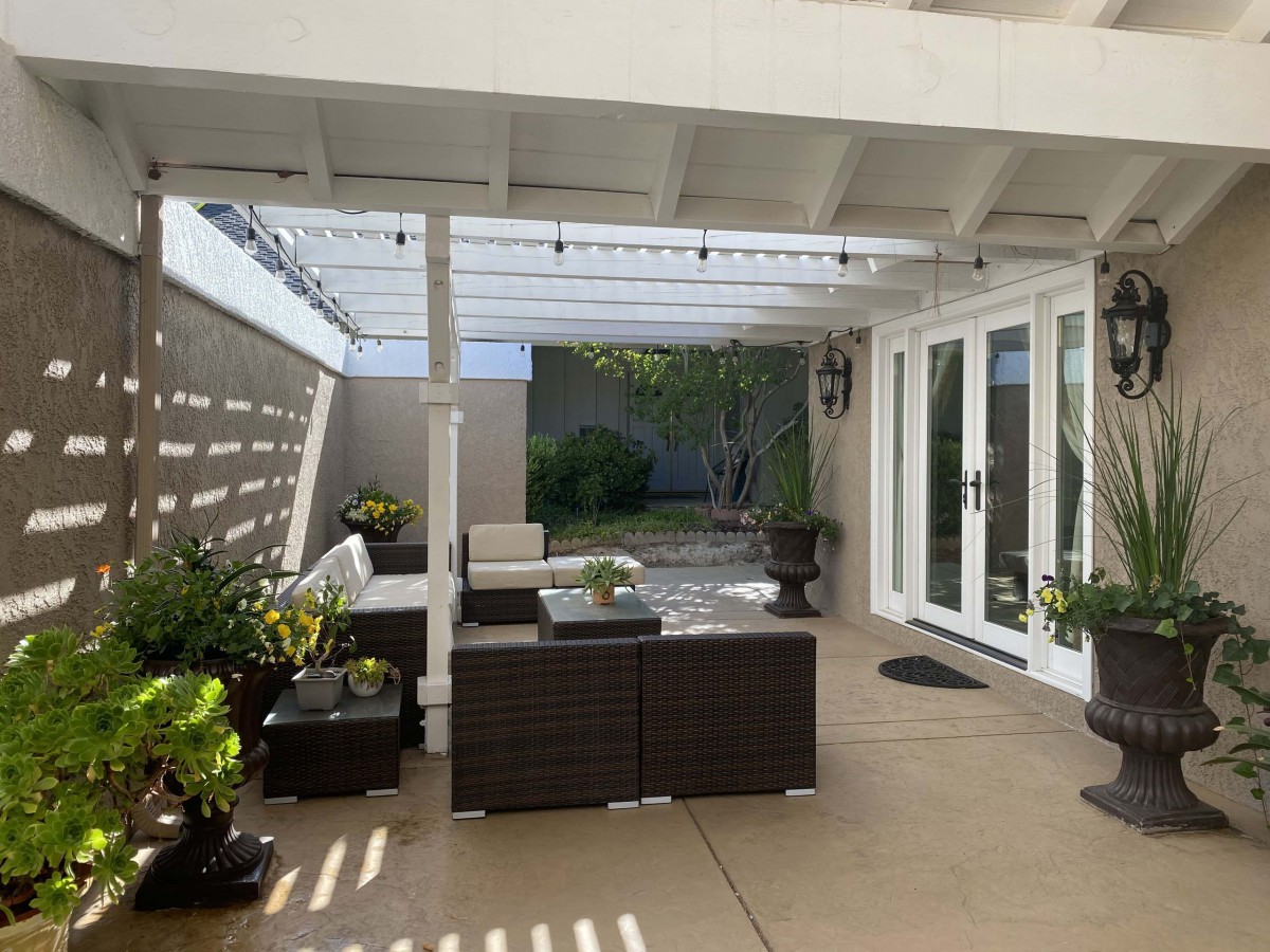 A cozy outdoor patio with wicker furniture under a pergola adorned with string lights.