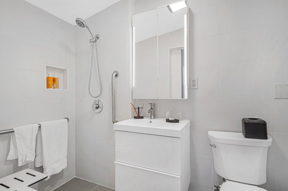 A modern, minimalist bathroom featuring a sleek shower, vanity with mirror, and a toilet.