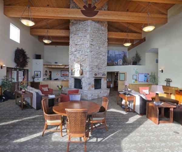 A lobby interior featuring a large stone fireplace, wooden ceiling beams, and seating area with tables and chairs.