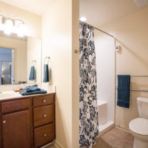 A well-lit bathroom featuring a vanity with a mirror, a shower with a patterned curtain, and neatly hung towels.