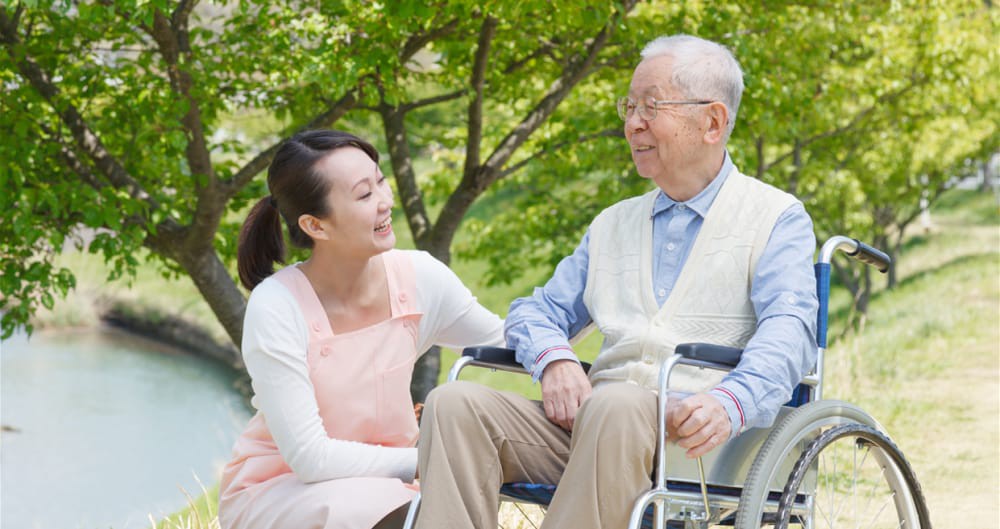 A woman interacts with an elderly man in a wheelchair outdoors.