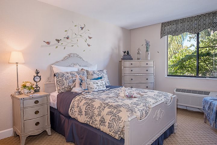 A cozy bedroom with elegant decor, featuring a white and blue color scheme and ample natural light.
