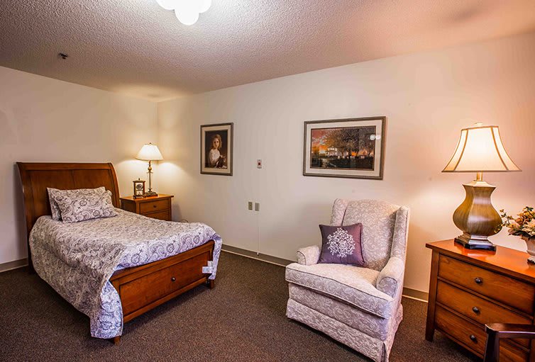 A cozy bedroom with a bed, armchair, and decorative paintings.