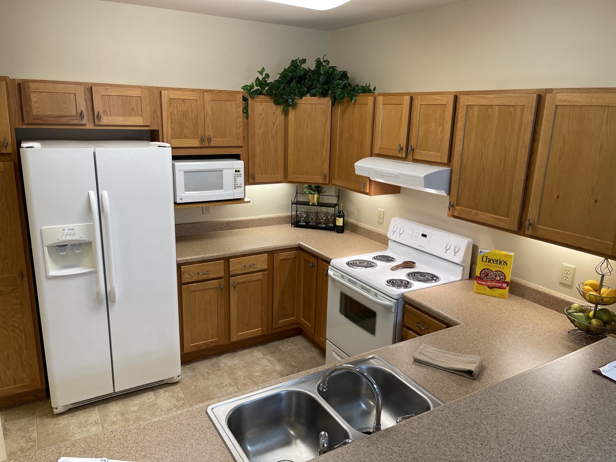 A clean and organized kitchen with wooden cabinets, a stove, fridge, microwave, and dual sink.