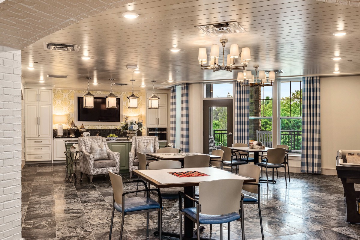 A modern and spacious dining area with elegant chandeliers, featuring tables and comfortable chairs, well-lit by natural light.