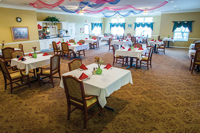 An elegantly decorated dining room with neatly arranged tables and chairs, featuring red table napkins and decorative ceiling drapes.