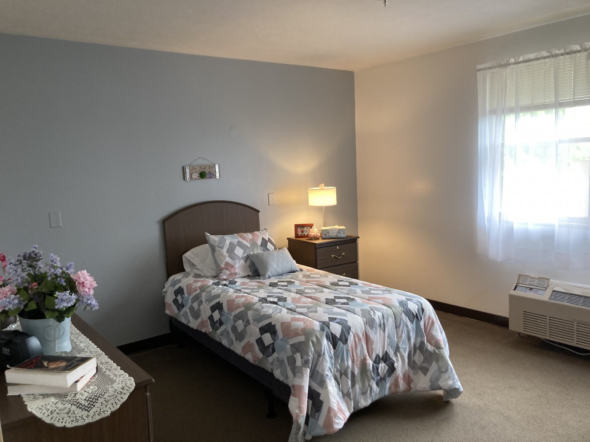 A cozy bedroom with a single bed, nightstand, and a lamp by the window.
