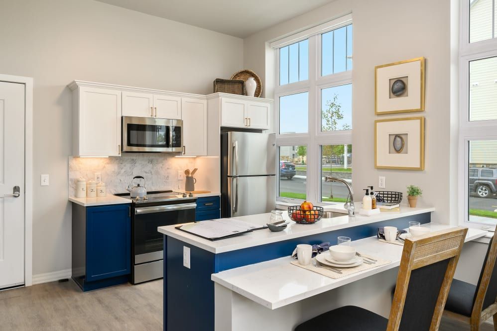 A modern kitchen interior featuring an island counter, stainless steel appliances, and ample natural light.