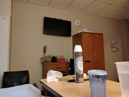 A view of a hospital room with a television, clock, and some items on the table.