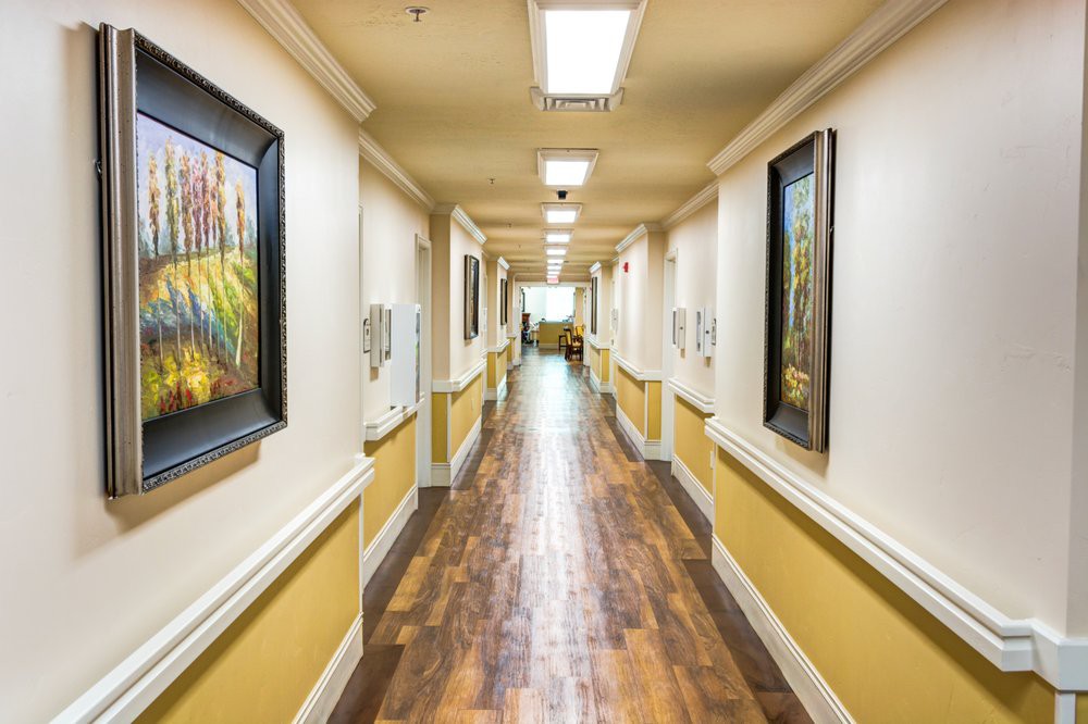 A well-lit hallway featuring wooden floors and adorned with paintings on the walls.