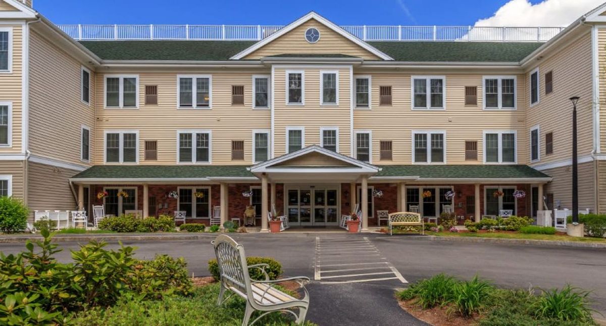A three-story residential building with a landscaped entrance and benches.
