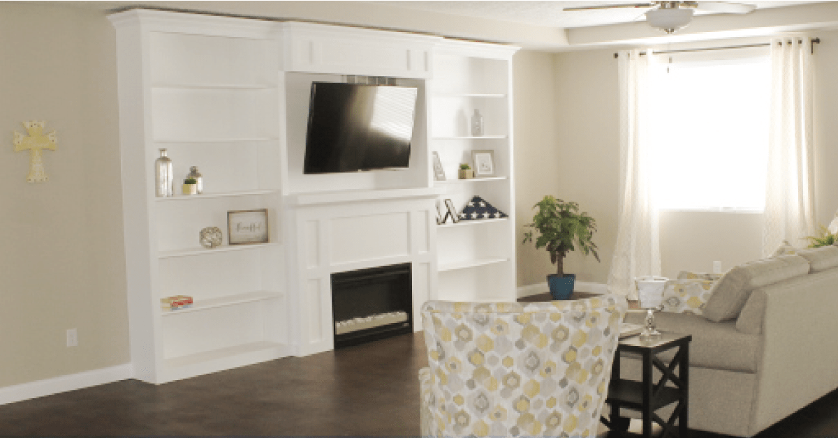 A cozy living room featuring a mounted television above a fireplace, surrounded by built-in bookshelves and tasteful decor.