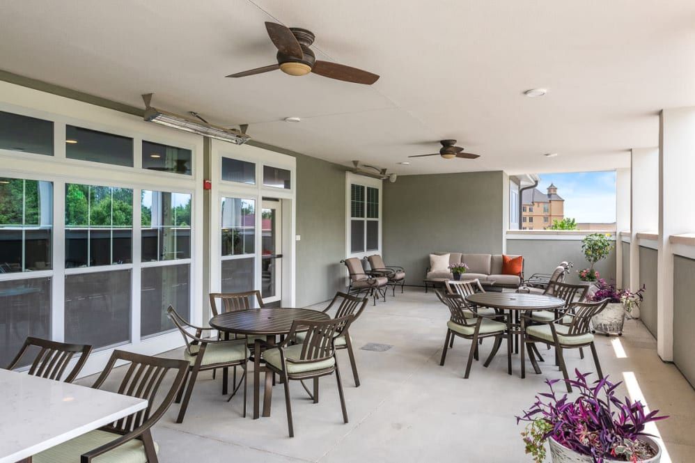 A covered outdoor patio area with tables, chairs, ceiling fans, and floral decorations.
